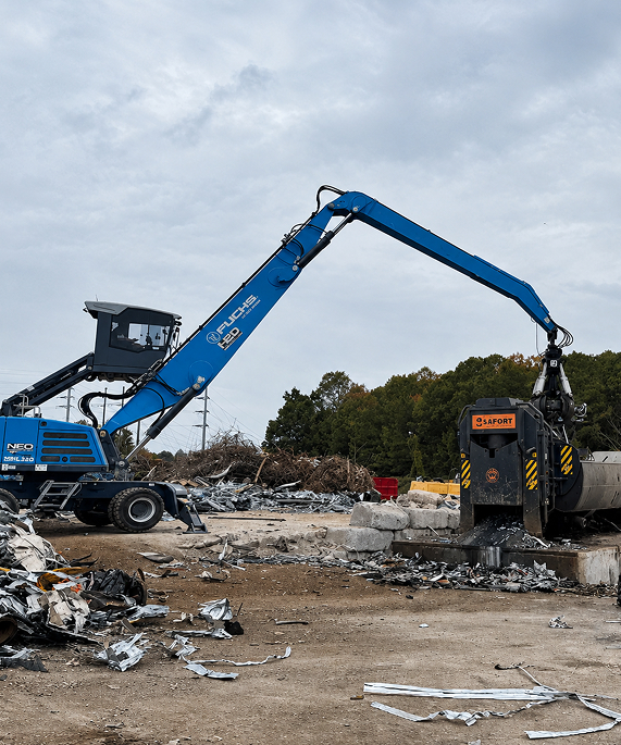 material-handler-with-shear-attachment-scrap-yard Blue material handler with a hydraulic shear attachment working among scrap metal at a recycling yard